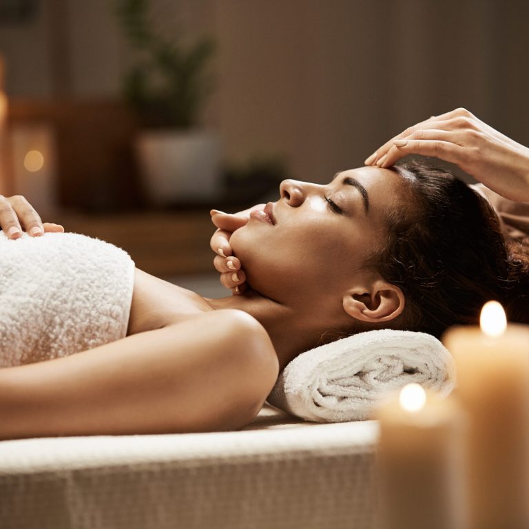 Attractive african girl enjoying face massage in spa salon. Closed eyes.