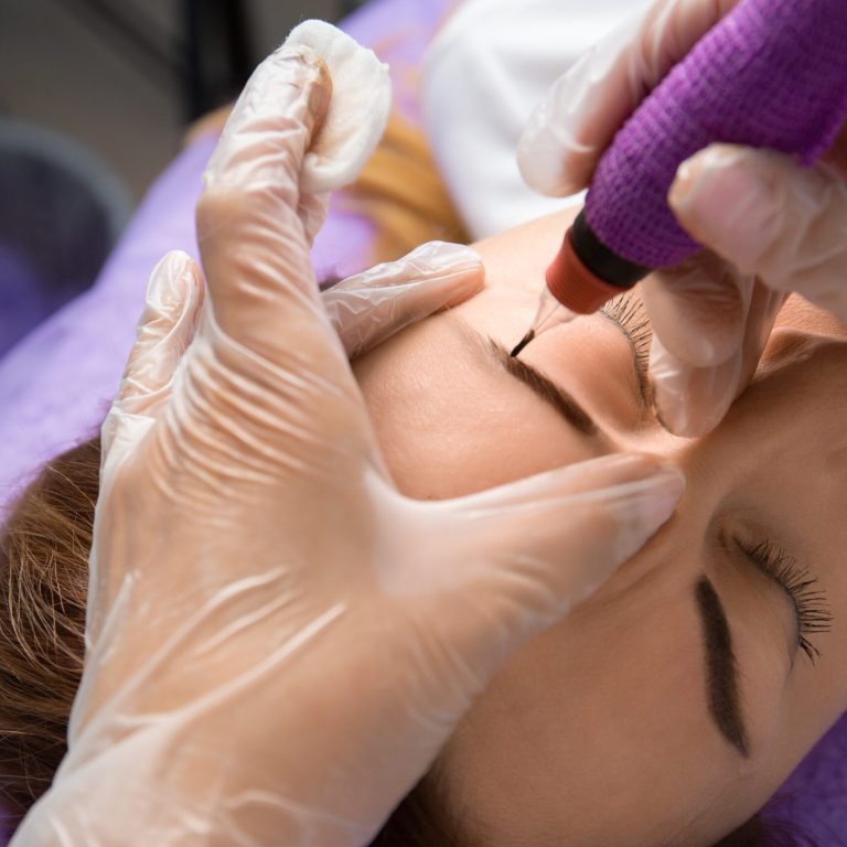 Beauty master performs permanent eyebrow makeup in a beauty salon, close-up. Hands of a cosmetologist doing microblading of eyebrows. Tattoo on the face.